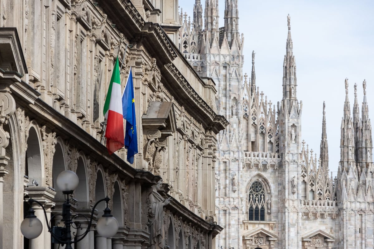 Italienflagge an einer verzierten Fassade mit den Spitztürmen des Mailänder Doms im Hintergrund