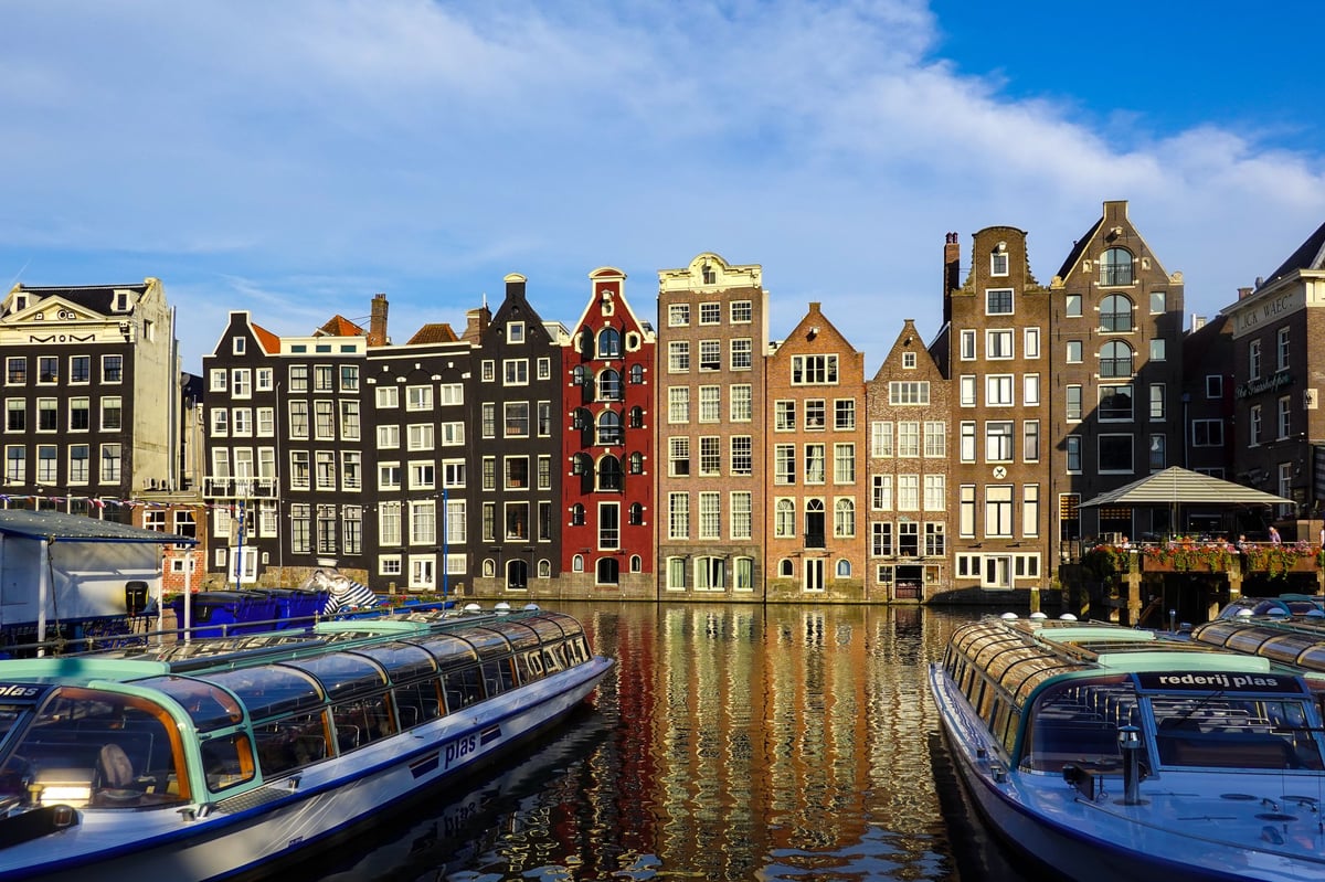 Reihe bunter historischer Grachtenhäuser in Amsterdam, gespiegelt im Wasser, mit festgemachten Booten im Vordergrund