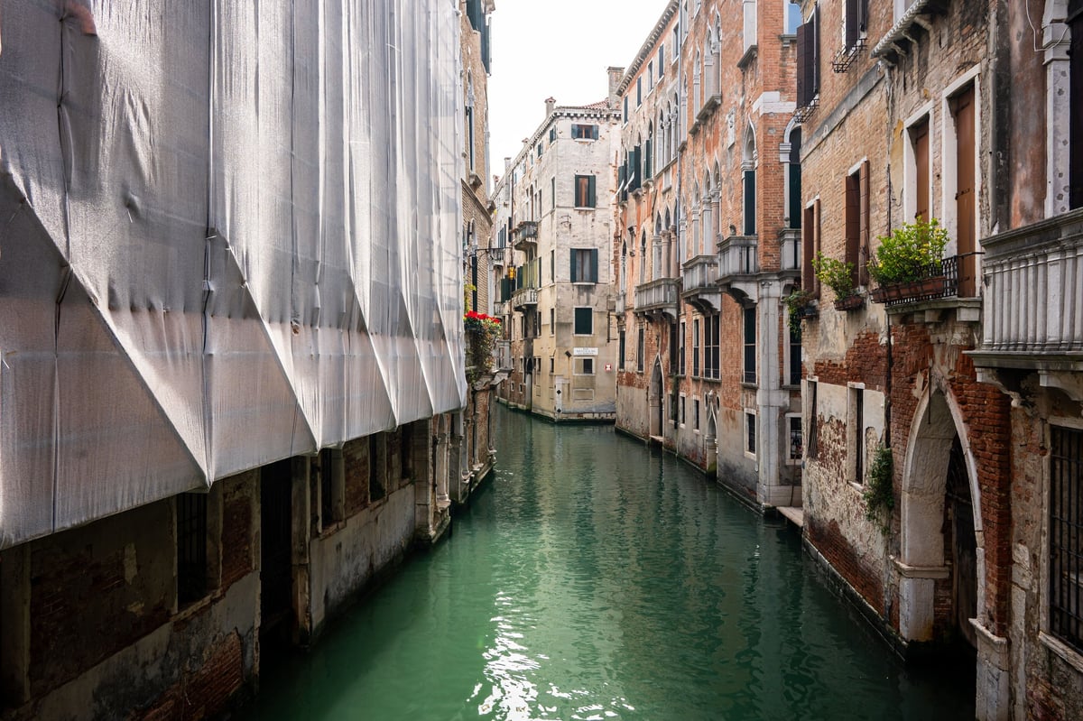 Schmaler Kanal in Venedig mit grünem Wasser, flankiert von historischen, verwitterten Häusern und einem weißen Boot am linken Ufer
